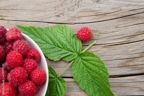 ripe raspberries with leaves and flowers on a wooden table.Space for text.