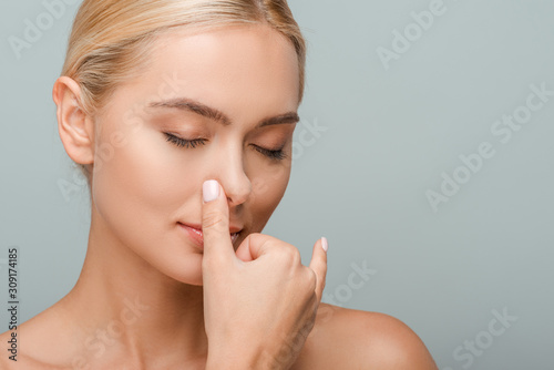 beautiful girl with closed eyes touching nose isolated on grey
