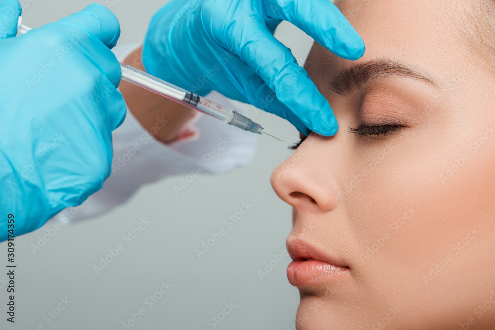 cropped view of cosmetologist making beauty injection to attractive woman isolated on grey cropped view of cosmetologist making beauty injection to attractive woman isolated on grey