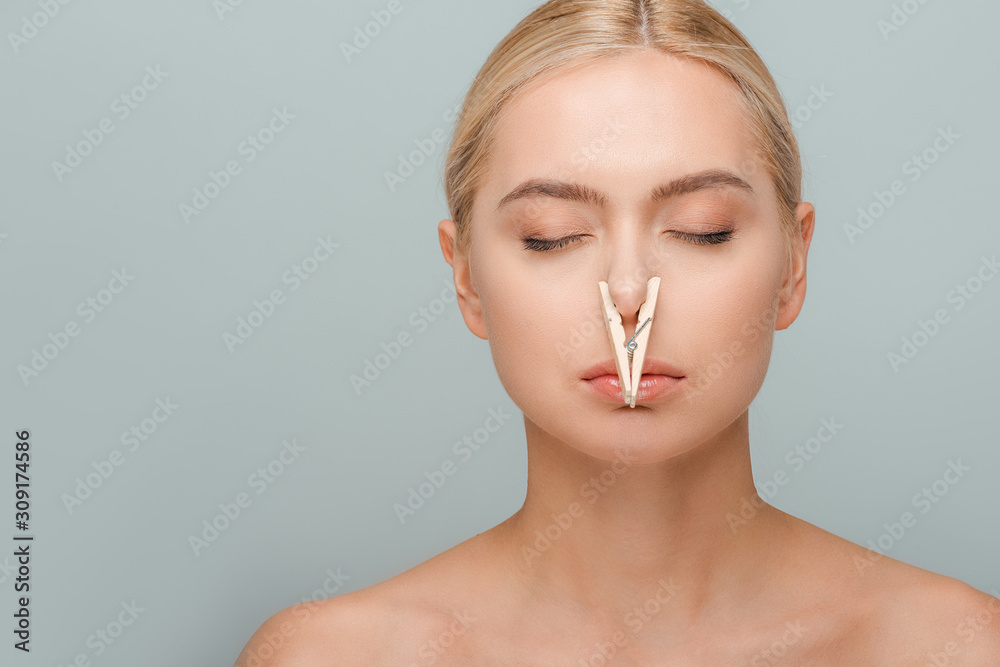attractive and naked young woman with wooden pin on nose and closed eyes isolated on grey - obrazy, fototapety, plakaty 