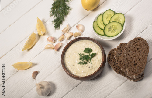Top view of tzatziki sauce with greenery  cucumber and lemon on white wooden background