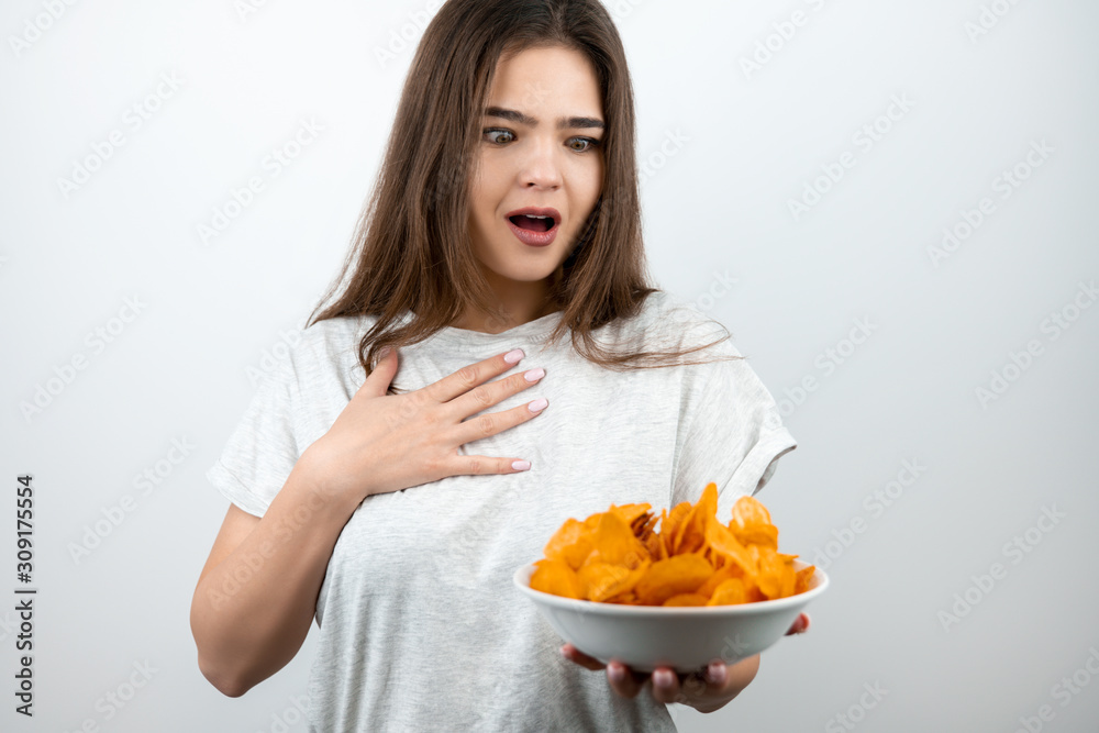 young attractive woman holding plate with spicy potatoe chips looking astonished on isolated white background dietology and nutrition young attractive woman holding plate with spicy potatoe chips looking astonished on isolated white background dietology and nutrition