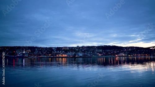 Tromso city, view of Tromso bridge, harbour and city centre from across the fjord, at night during blue hour light.