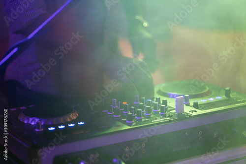 club dj plays music on stage in nightclub.Hand of disc jockey adjusting sound track volume level.Professional audio equipment on music festival