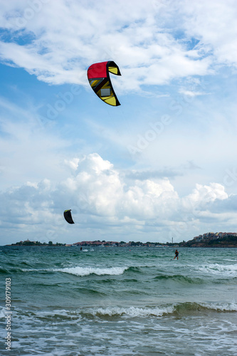 Kite surf ride his hydrofoil kite through surfing waves on sea.  Kitesurfers ride kites on Black Sea at sandy Beach In Bulgaria, Sozopol on sunny day at sunset on blue sky and clouds background.