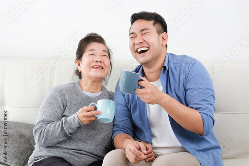 Asian senior grand mother and son drinking coffee and talking happy and smile face in living room