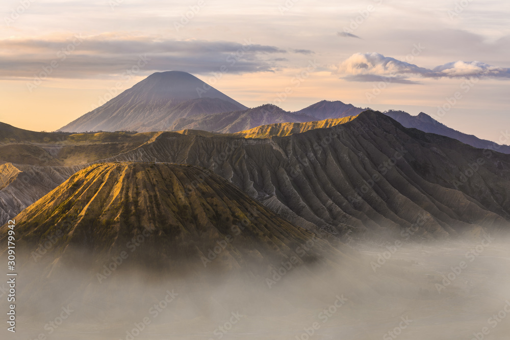 View from above, stunning close-up view of the Mount bromo crater and the Mount Batok surrounded by clouds during sunrise. Mount Semeru in the background, east Java, Indonesia.