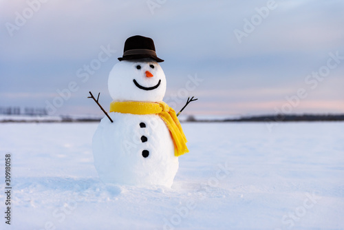 Fototapeta Funny snowman in stylish black hat and yellow scalf on snowy field