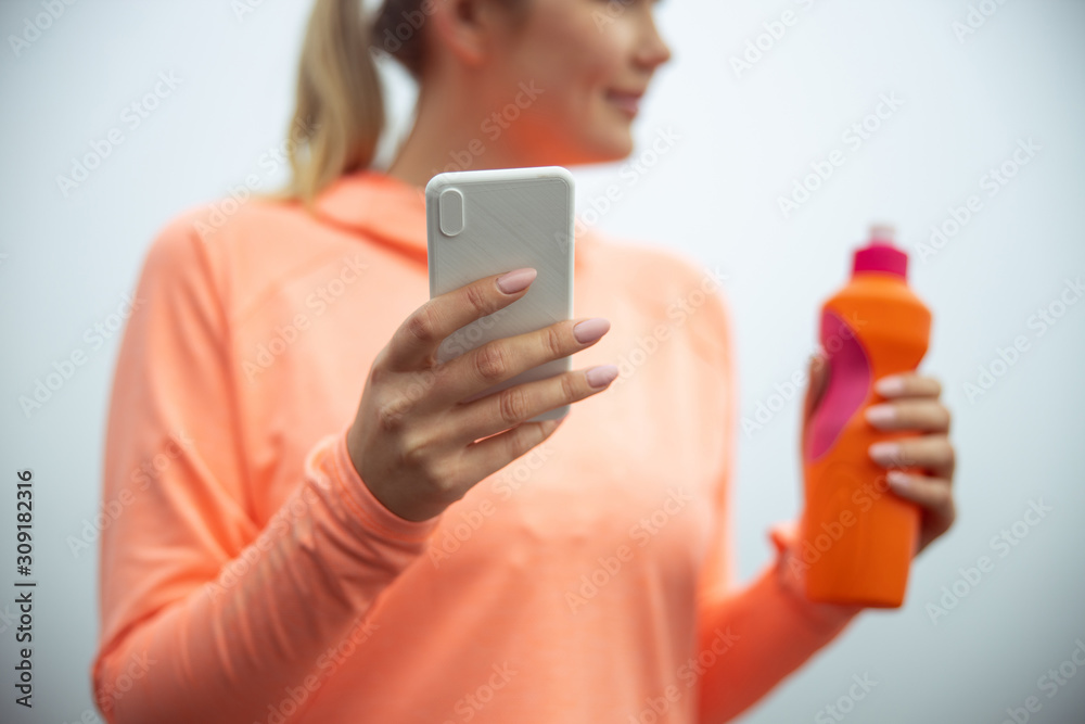 Fototapeta premium Young woman holding modern smartphone and bottle of water