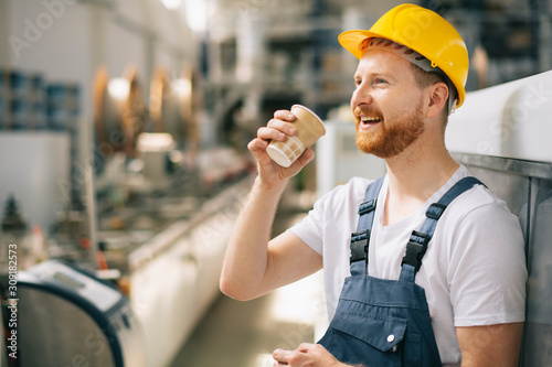 Portrait of young worker drinking coffee in factory.
