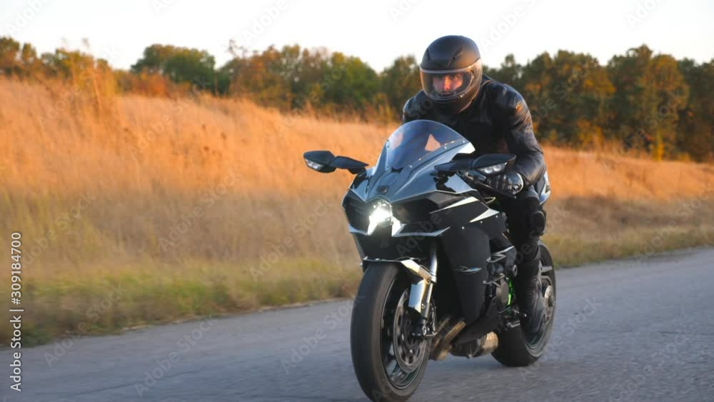 Motorcyclist racing his motorcycle on autumn country road. Young man in helmet riding fast on modern sport motorbike at highway. Guy driving bike during trip. Concept of freedom. Front view Close up