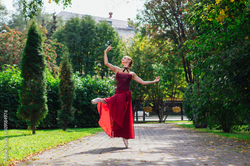 Woman ballerina in red ballet dress dancing in pointe shoes in autumn park. © Smile