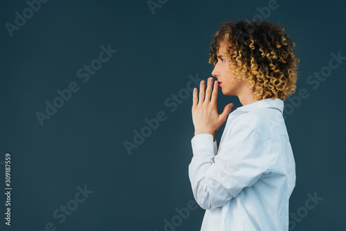 side view of curly teenager in total white outfit with praying hands isolated on green