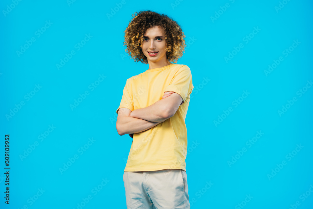 smiling curly teenager with crossed arms isolated on blue smiling curly teenager with crossed arms isolated on blue