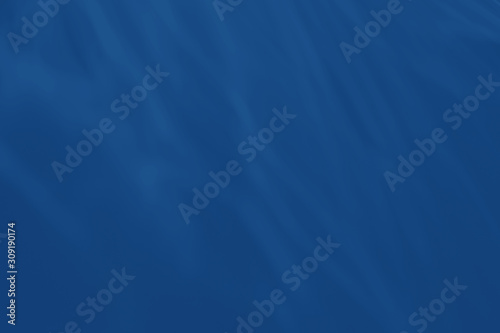Trendy blue colored low contrast abstract background with light and shadows caustic effect. Light passes through a glass. Water background. 2020 year color trend