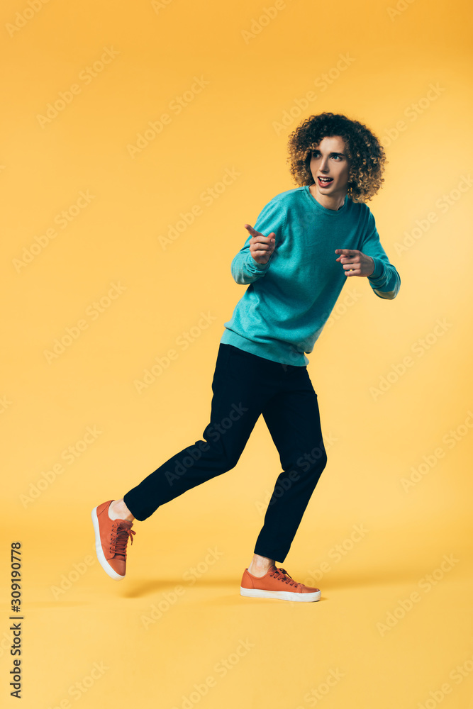 full length view of curly teenager running and pointing with fingers on yellow