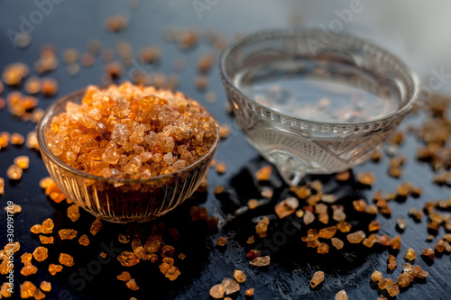 Gond katara/Gond Katira/ Tragacanth Gum or edible gum in a glass bowl along with some water in another bowl for relief in back pain. On a black glossy surface with some spread gond crystals.