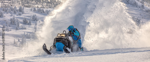 Pro snowmobiler makes a turn and lets a flurry of snow spray from under the caterpillar. sports snowmobile in the mountains. bright skidoo motorbike and suit without brands. Winter fun moto extreme photo