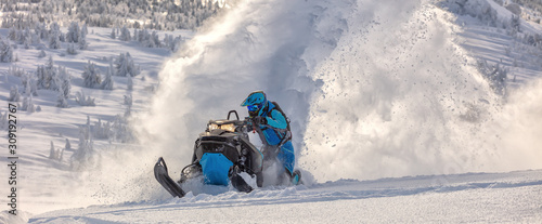 Pro snowmobiler makes a turn and lets a flurry of snow spray from under the caterpillar. sports snowmobile in the mountains. bright skidoo motorbike and suit without brands. Winter fun moto extreme