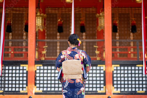 Geishas girl wearing Japanese kimono among red wooden Tori Gate at Fushimi Inari Shrine in Kyoto, Kimono is a Japanese traditional garment. The word "kimono", which actually means a "thing to wear"