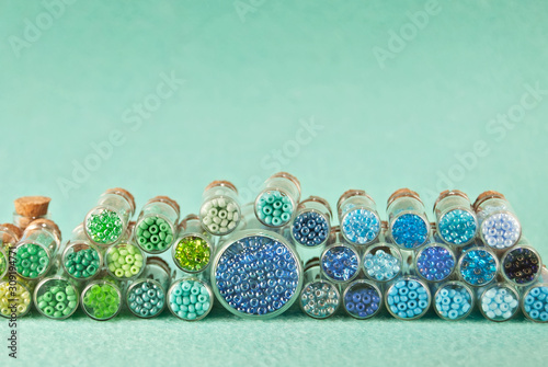 Fototapeta Blue, green, yellow and purple beads in glass jars on a bright cyan background