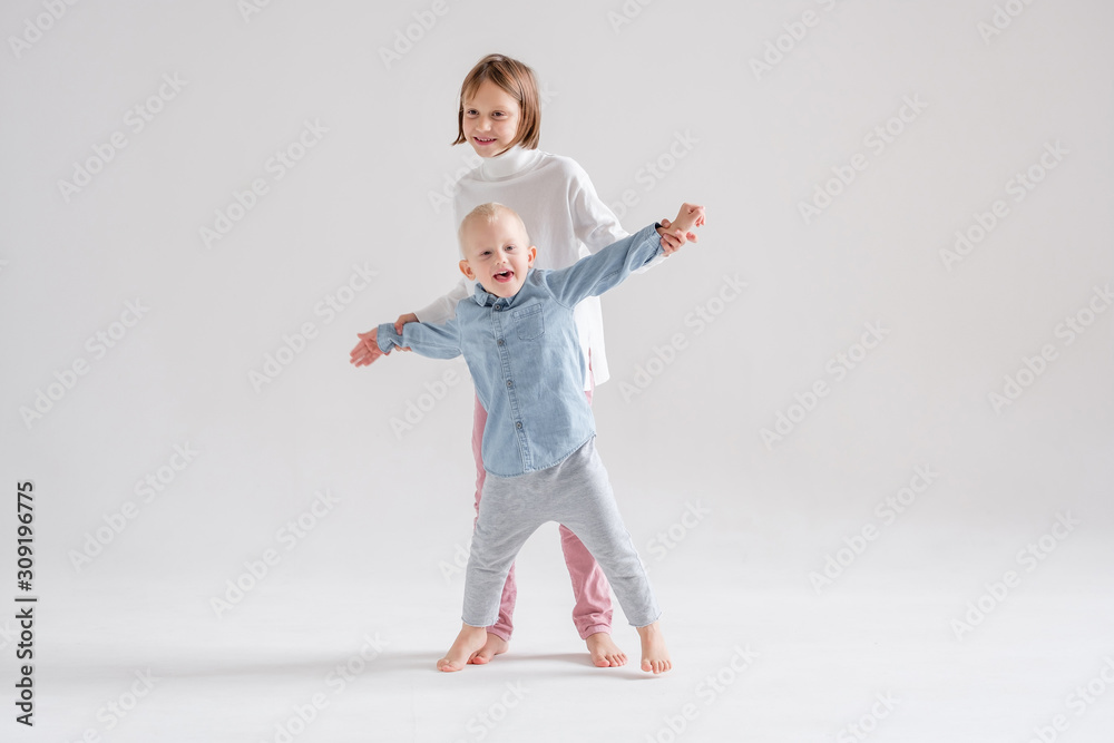 Positive older sister and brother communicate and play together in a cozy studio on a white background barefoot. Concept of happy friendly children. Advertising space