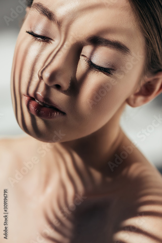 Fotografia portrait of naked girl with closed eyes and shadows on face on grey