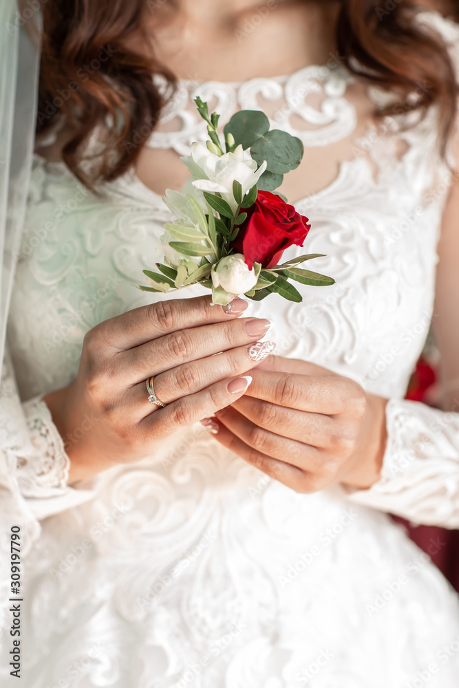 Close-up of the bride's hands holds a boutonniere. boutonniere with red rose.Beautiful sensual bride holding stylish boutonniere