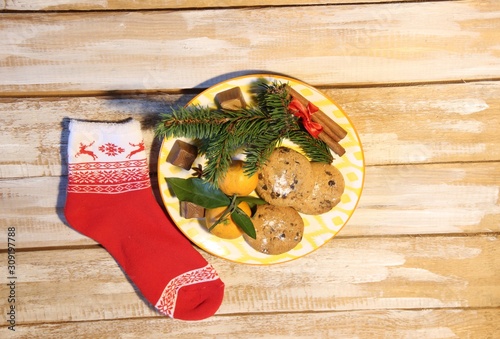Plate with new year cookies, mandarin, fir branch, cinnamon sticks, sweets, christmas cokc on wooden background photo