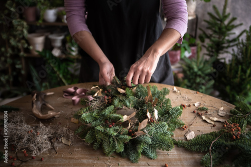Woman making Christmas wreath of spruce, step by step. Concept of florist's work before the Christmas holidays..