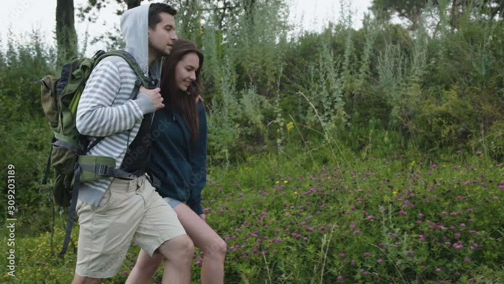 Happy couple in embraces with backpack walks on the path of field nature
