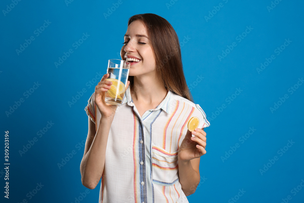 Young woman drinking lemon water on light blue background Young woman drinking lemon water on light blue background