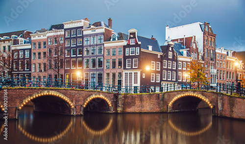 Amsterdam canal, bridge and typical houses, boats and bicycles during evening twilight blue hour, Holland, Netherlands