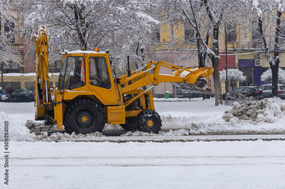 Yellow tractor with snowplow removing snow from the streets. 