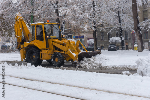 Yellow tractor with snowplow removing snow from the streets. 