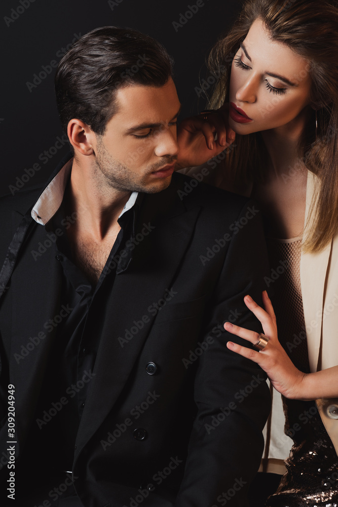 attractive woman hugging handsome man in suit isolated on black