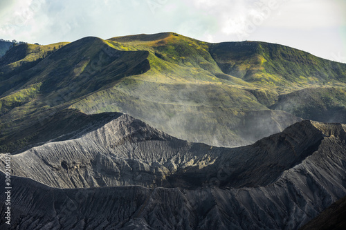 Stunning close-up view of the Mount bromo crater in the foreground and beautiful green hills illuminated by sunset in the background. Mount Bromo is an active volcano in East Java, Indonesia. photo