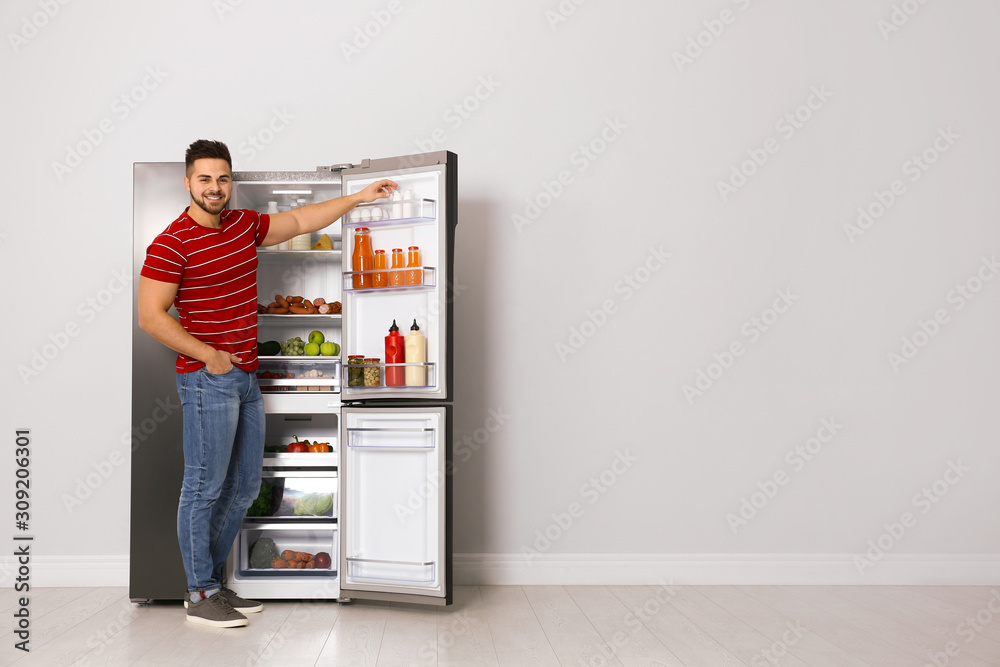 Young man taking yoghurt out of refrigerator indoors, space for text Young man taking yoghurt out of refrigerator indoors, space for text