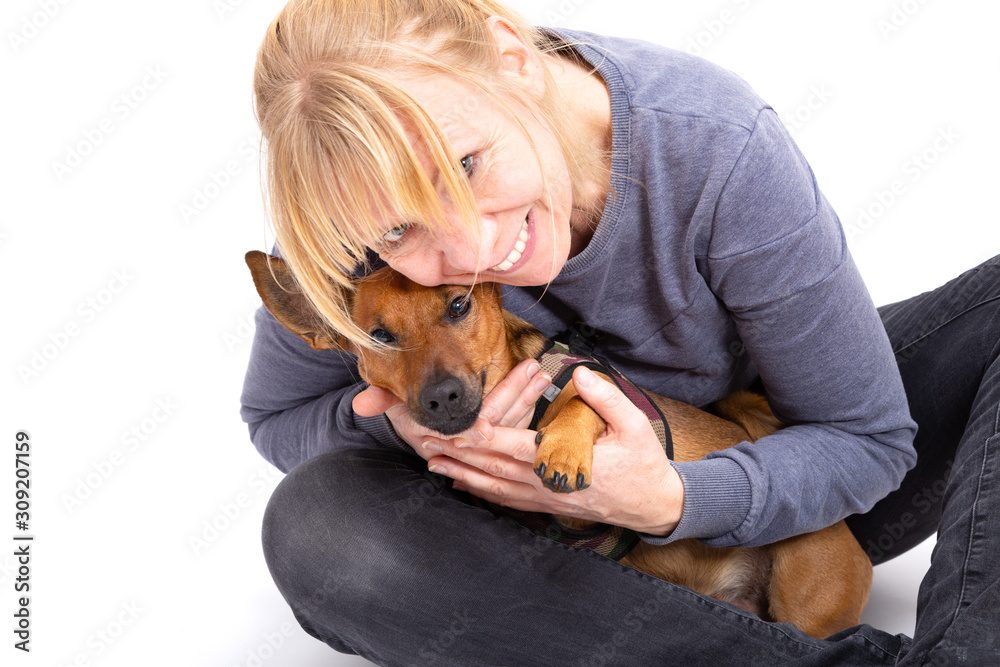 Blonde woman sitting on the floor with her tiny brown dog isolated on white background in the studio.  Small mixed breed of jack russell terrier, german shepherd and chihuahua. Age 2 years.