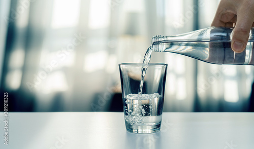 Nalewanie oczyszczonej świeżej wody do picia z butelki na stole w salonie © piotrszczepanek