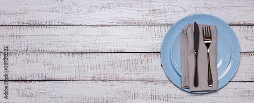 Blue plates, napkin and cutlery on an old white wooden background.