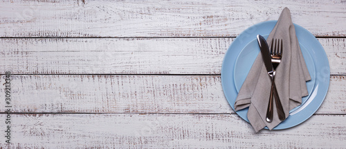 Blue plates, napkin and cutlery on an old white wooden background.