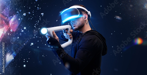 Beautiful man over dark magic background. Gamer guy in glasses of virtual reality with controllers in hands. Augmented reality, game, hobby concept. VR. Blue neon light.