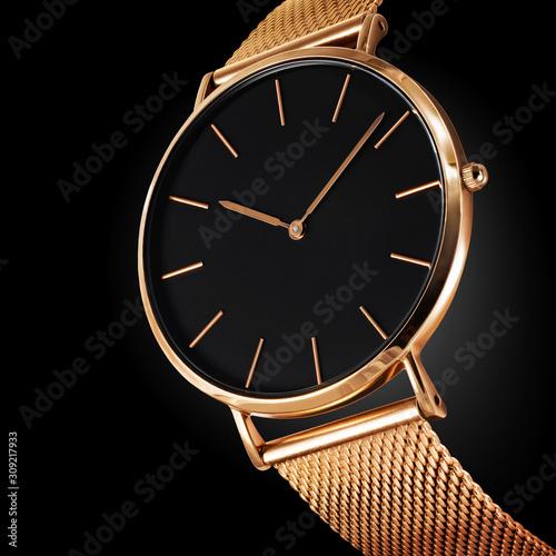 Close up of an expensive wristwatch made of gold metal and isolated on a black background photo