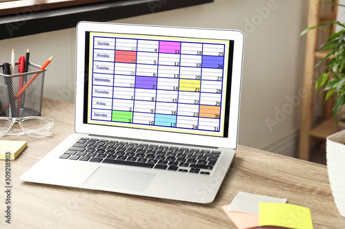 Modern laptop with calendar app at table in office © New Africa