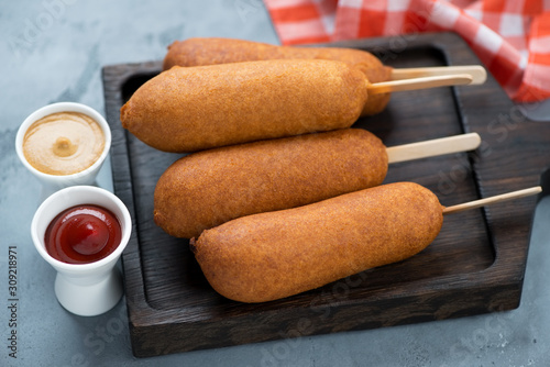 Corn dogs on a black wooden serving board with mustard and ketchup, studio shot, closeup photo