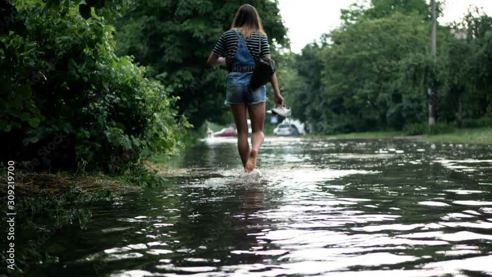 Girl barefoot in dirty water on the flooded city street after heavy rain. Disaster flood deluge and water flow after rainfall. Natural weather disaster-cataclysm Girl barefoot in dirty water on the flooded city street after heavy rain. Disaster flood deluge and water flow after rainfall. Natural weather disaster-cataclysm