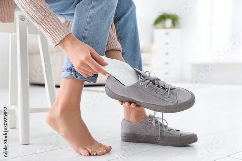 Woman putting orthopedic insole into shoe at home, closeup photo