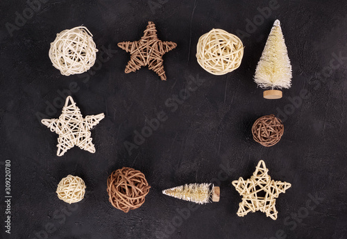 Christmas holiday background: frame of wicker stars and balls, little firs on a black textured background. Place for text. Top view. Flat lay