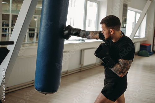 MMA and boxing training. Brutal, tattooed man boxing in a MMA training session in the gym. © Mihail